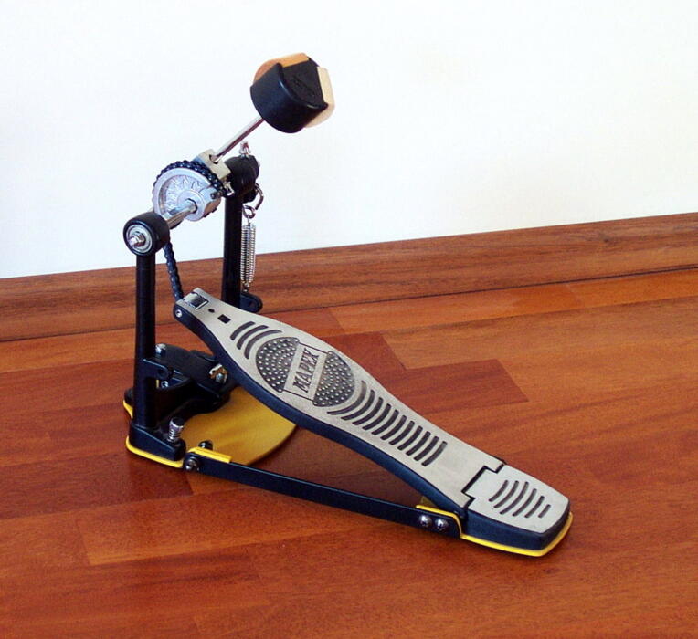 Close-up of a drum pedal showing the footboard, beater, and spring mechanism. Source: Wikimedia Commons.