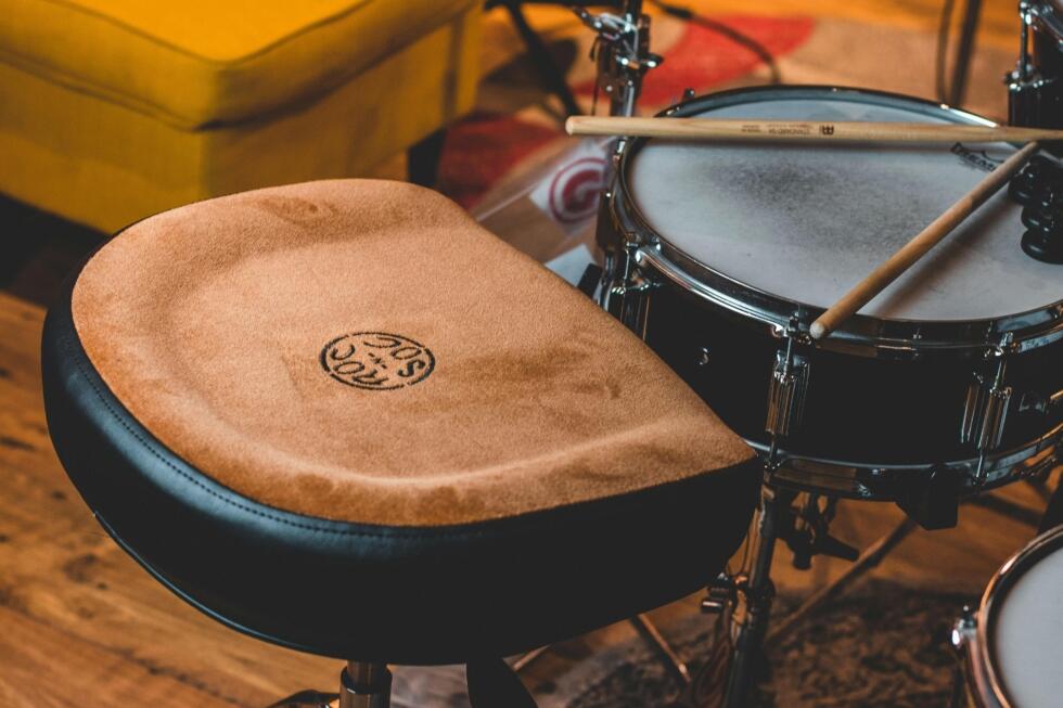 Adjustable drum throne with padded seat and sturdy metal base, designed for drummers’ comfort and posture during long sessions.