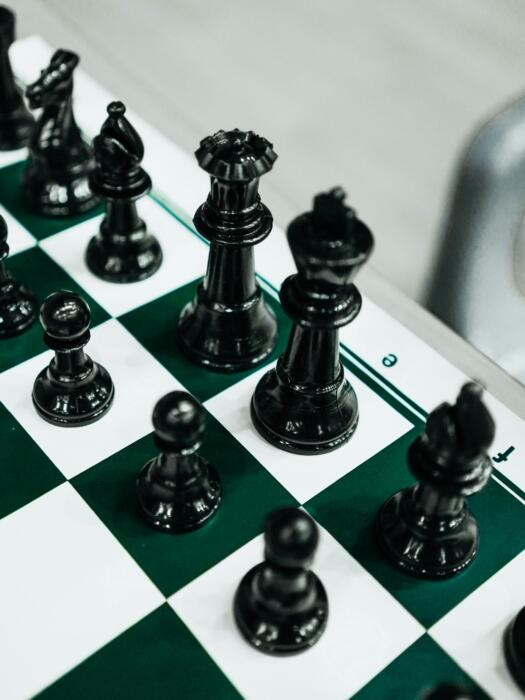 A close-up view of several chess pieces on a green and white board, with the focus on the central pieces while the background appears softly blurred.