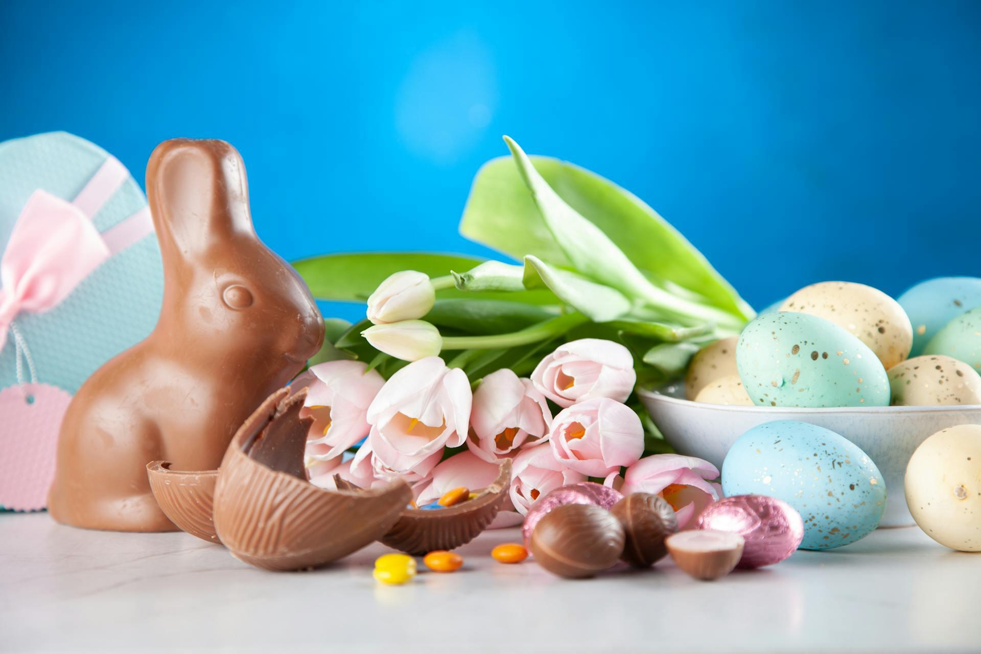 Chocolate bunny, pastel eggs, and pink tulips arranged against a blue background, celebrating Easter's festive ambiance.