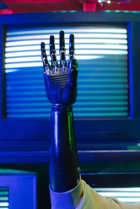 A robotic hand with detailed fingers reaches upward, set against a backdrop of retro screens with blue and green lighting.