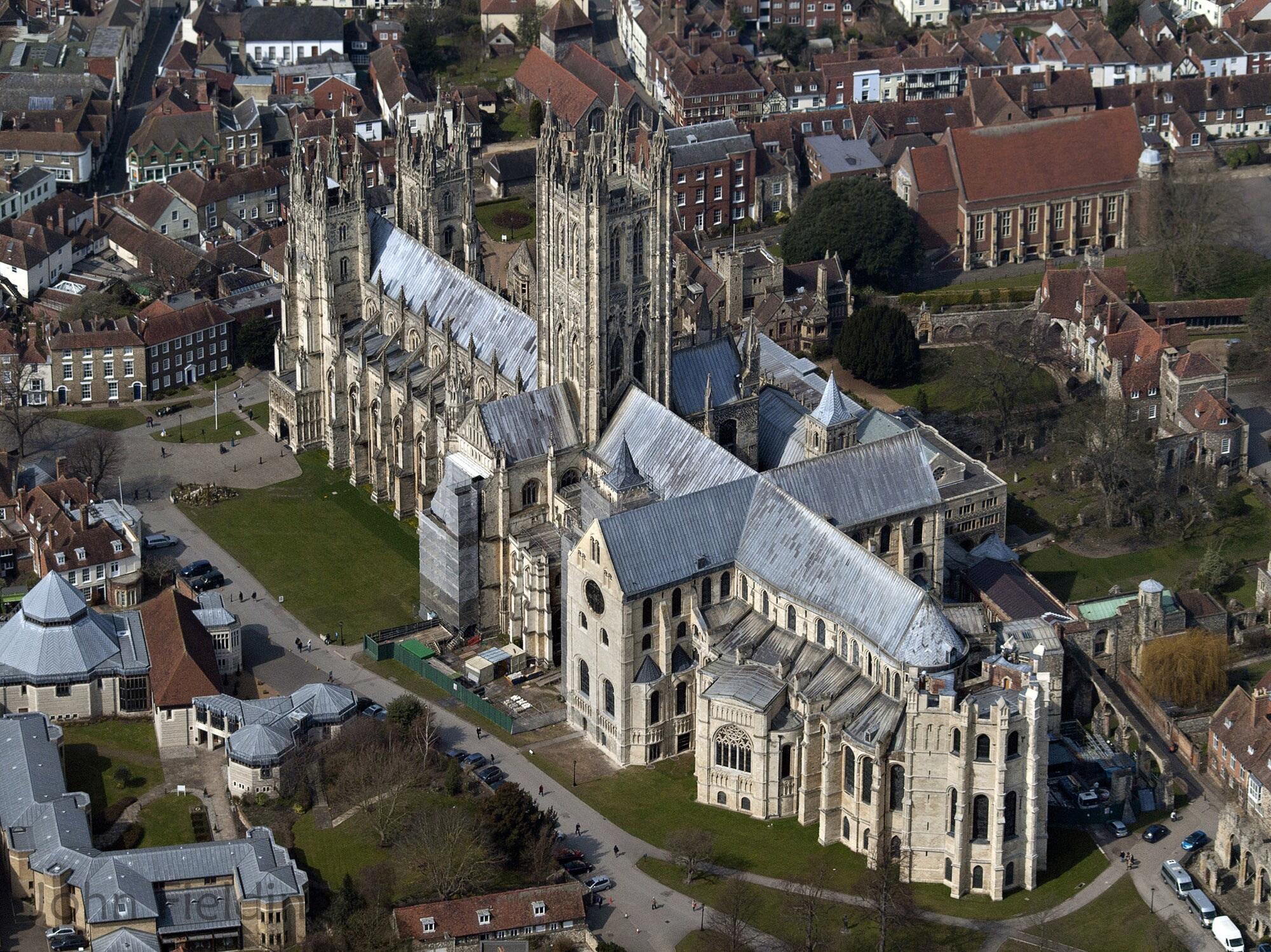 A large stone building seen from the air featuring towers, with green spaces and other building surrounding it.